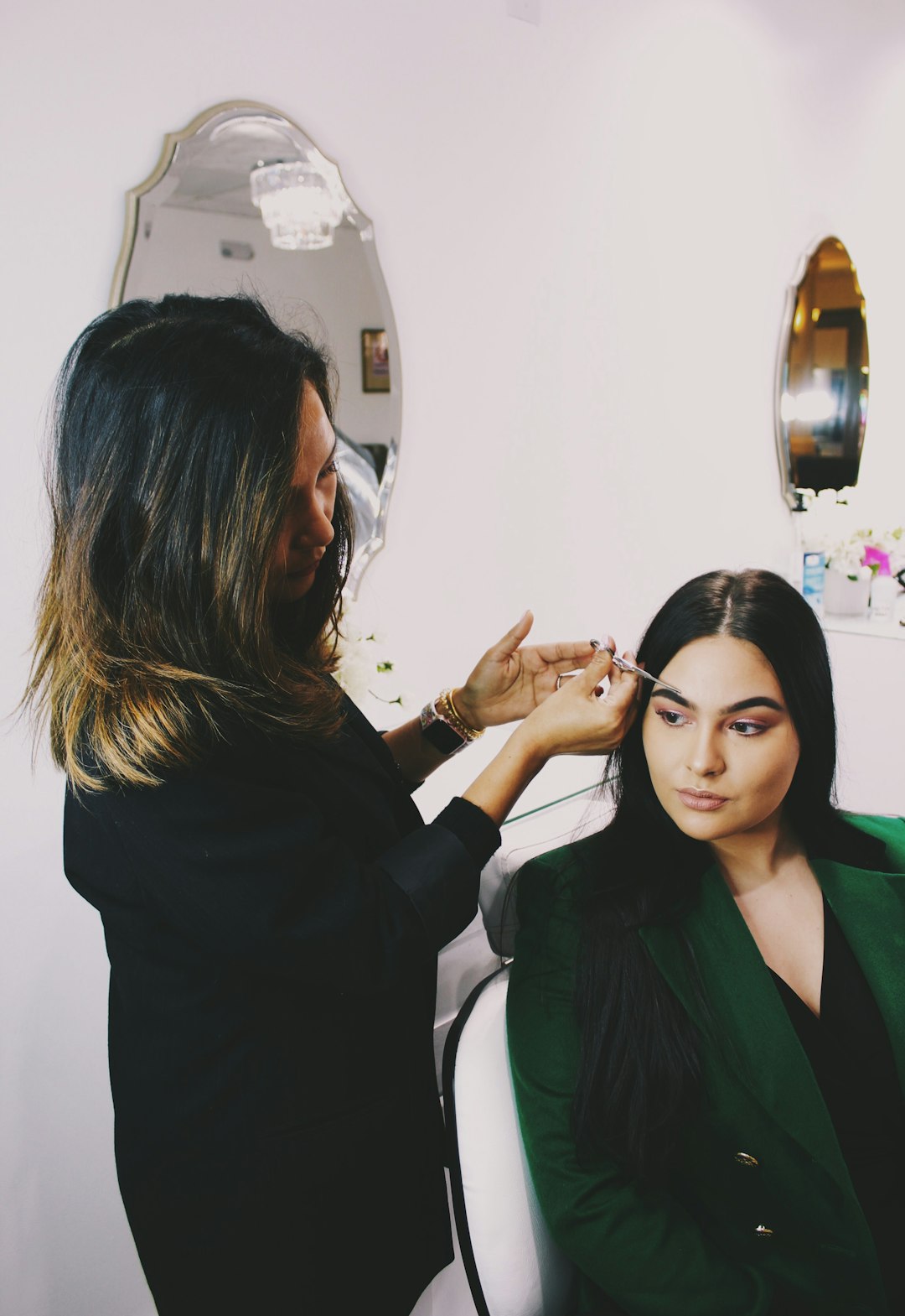 woman-clipping-eyebrow-of-woman-wearing-green-blazer-djhppewkrys